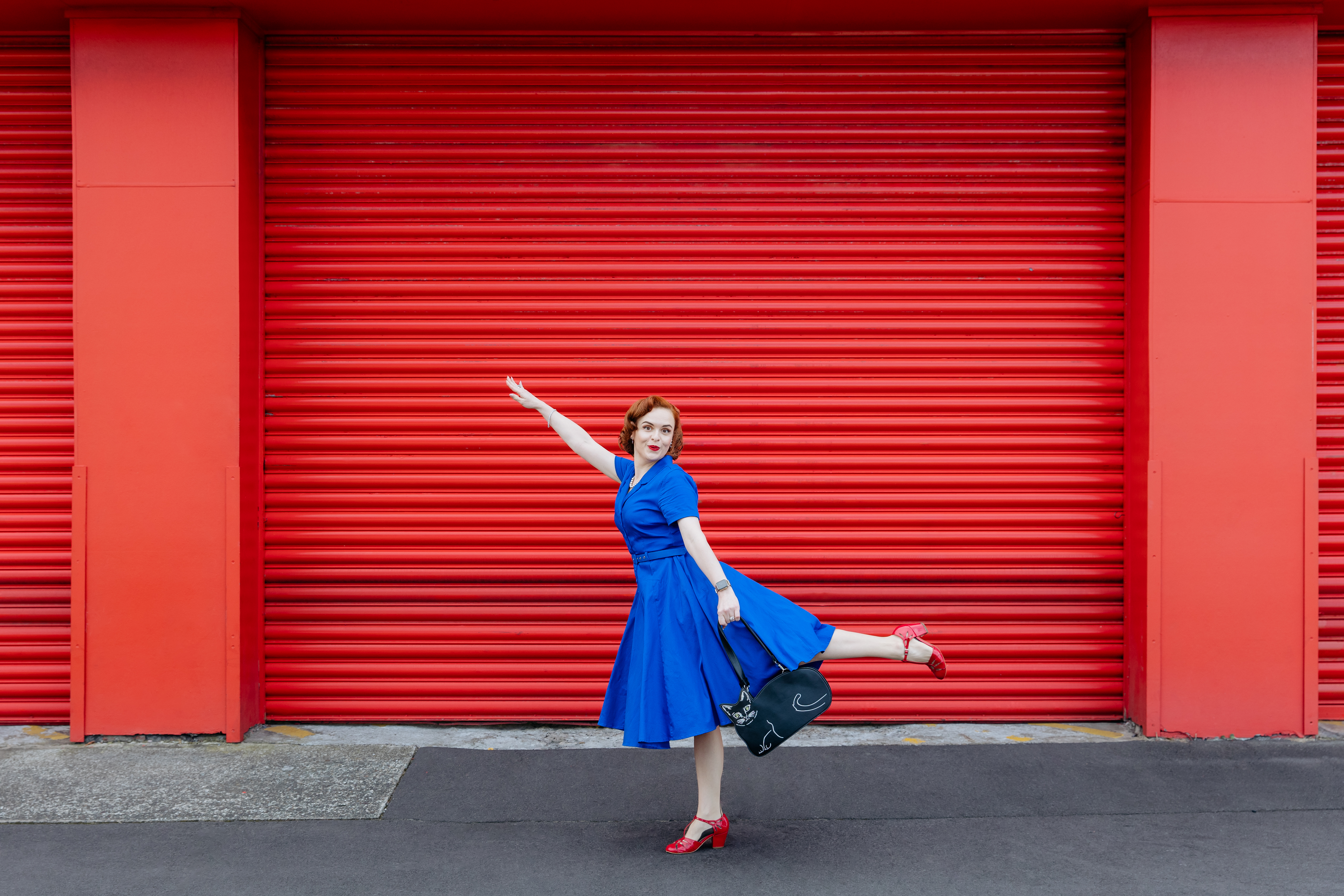 A woman in a blue dress with a cat bag in front of a red background gestures to move up, like a rocketship
